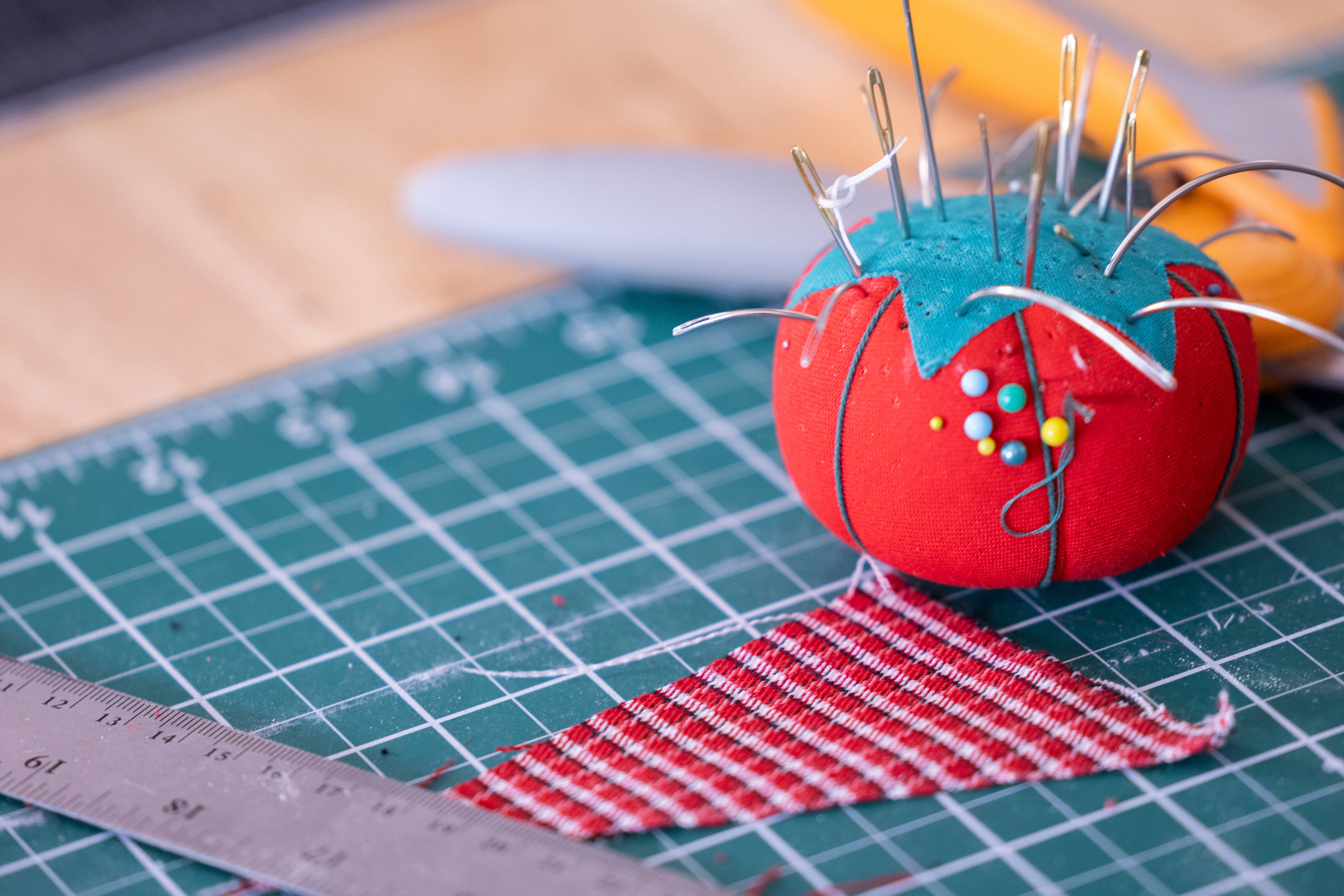 Tomato pin cushion laid on top of measuring tools and surrounded by fabric